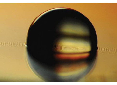 Figure 1: Photo shows a water droplet sitting on a ferrofluid-impregnated surface, which has cloaked the droplet with a very thin layer. Courtesy: Kripa Varanasi, Karim Khalil, Numan Abu-Dheir, Seyed Mahmoudi, MIT