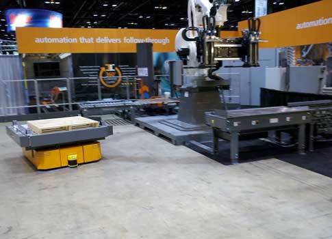 A mobile robot, left, moves a pallet from the palletizing area (back, right) to the picking area (front, right) at Pack Expo 2014 in Chicago. The mobile robot, with a conveyor section on top, is expected to be available from Intelligrated early in 2015. I