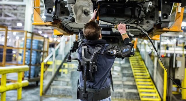 An exoskeleton helps support a worker’s upper body while he performs repetitive overhead work drilling underbody car panels. Courtesy: Motor Company/RIA