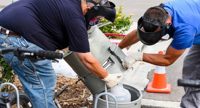 Physical Plant plumbers open a wastewater sampler from a COVID-19 wastewater surveillance site on campus to remove a sample for testing. Courtesy: Jeff Miller, University of Wisconsin-Madison