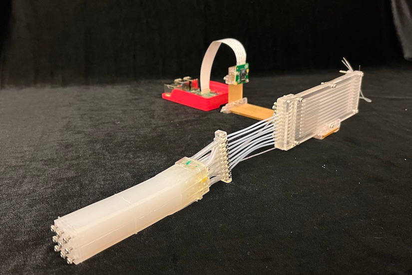 The researchers’ soft robotic device, an elastomeric finger containing nine fiber-based deformation sensors and a microfluidic pressure sensor, is shown with the display assembly and a digital camera. Together, the sensors can sense pressure, bending, elongation, and twist in the finger. Courtesy: Michael Wehner, University of Wisconsin-Madison