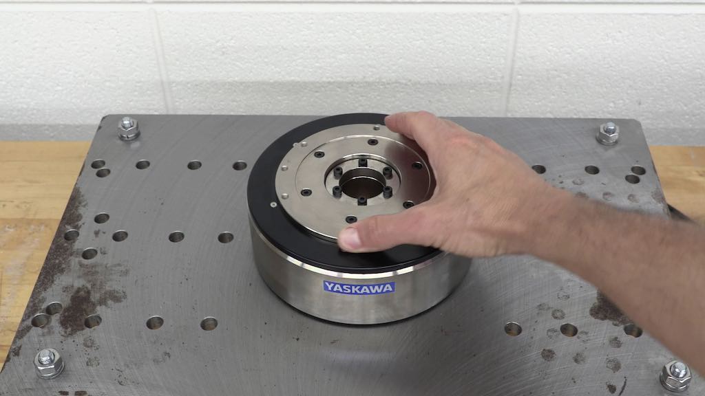 Figure 1 shows a typical direct-drive motor mounted on a steel plate, with a hand turning the rotating flange. Courtesy: Yaskawa America Inc.