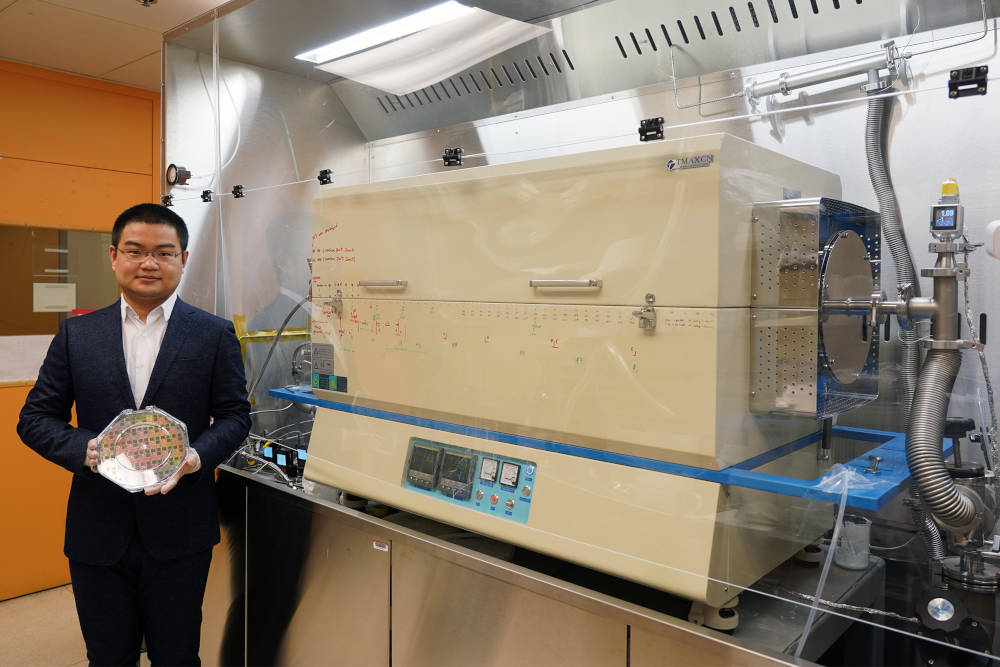 Graduate student Jiadi Zhu holding an 8-inch CMOS wafer with molybdenum disulfide thin film. On the right is the furnace the researchers developed, which enabled them to "grow" a layer of molybdenum disulfide onto the wafer using a low-temperature process that did not damage the wafer.Courtesy: Massachusetts Institute of Technology (MIT)