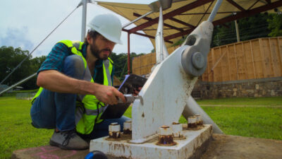 EIT Engineer Stefan Gosey on site using a caliper to measure the thickness of a guy wire anchor plate supporting a tension fabric structure in North Carolina.