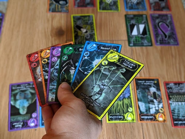 There are eighteen system cards representing six different cybersecurity domains, each having a different color. Your goal is to collect and protect these system cards, while attempting to compromise or steal them from other players. The card names follow right in line with standard cyber terminology such as a Zero Day attacks. That's a real cyberattack that you can read about in the game's user manual. You also have firewall cards that protect you from certain types of attacks. Courtesy: Scruffy City Games